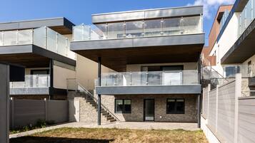A modern multi-story residential building with a flat roof, large windows, and a stone facade.