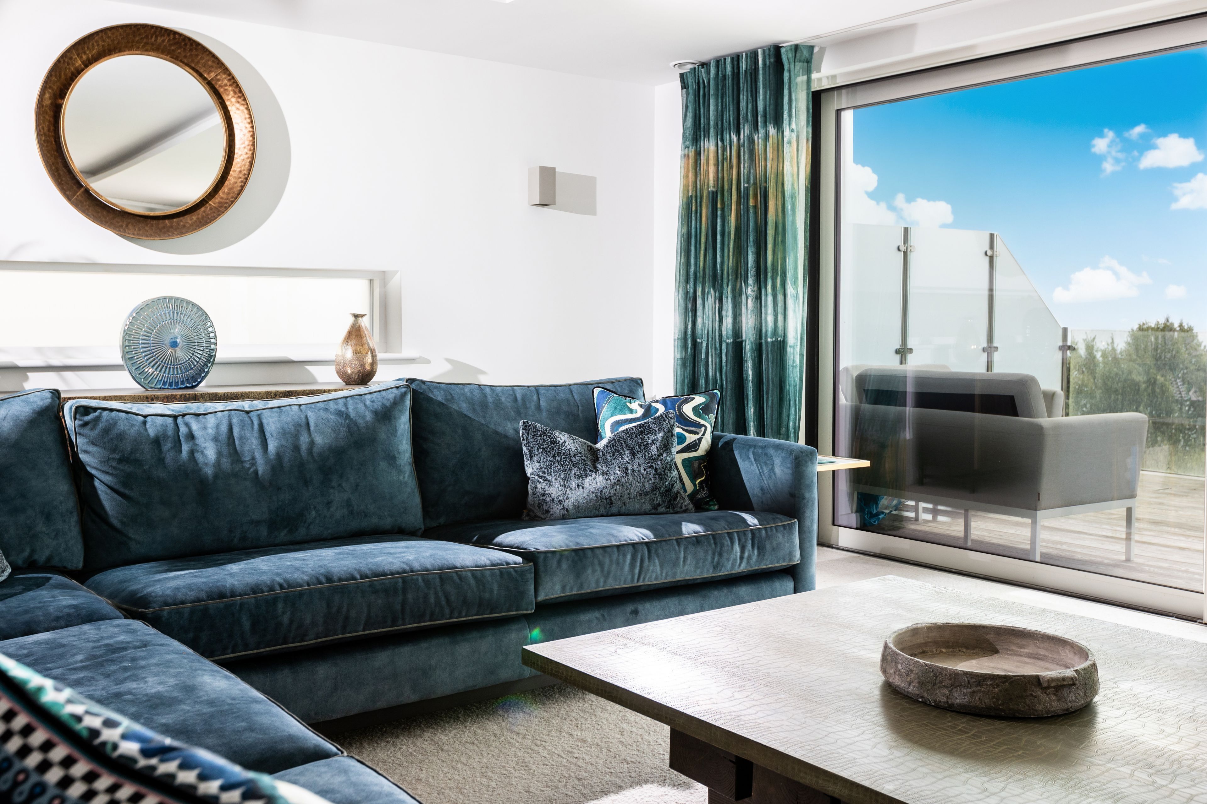 A modern living room with a sectional sofa, a coffee table, and a large window with a view of the sky.