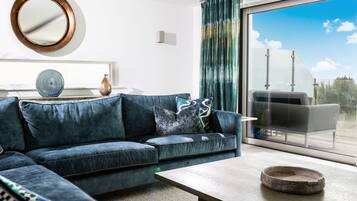 A modern living room with a sectional sofa, a coffee table, and a large window with a view of the sky.
