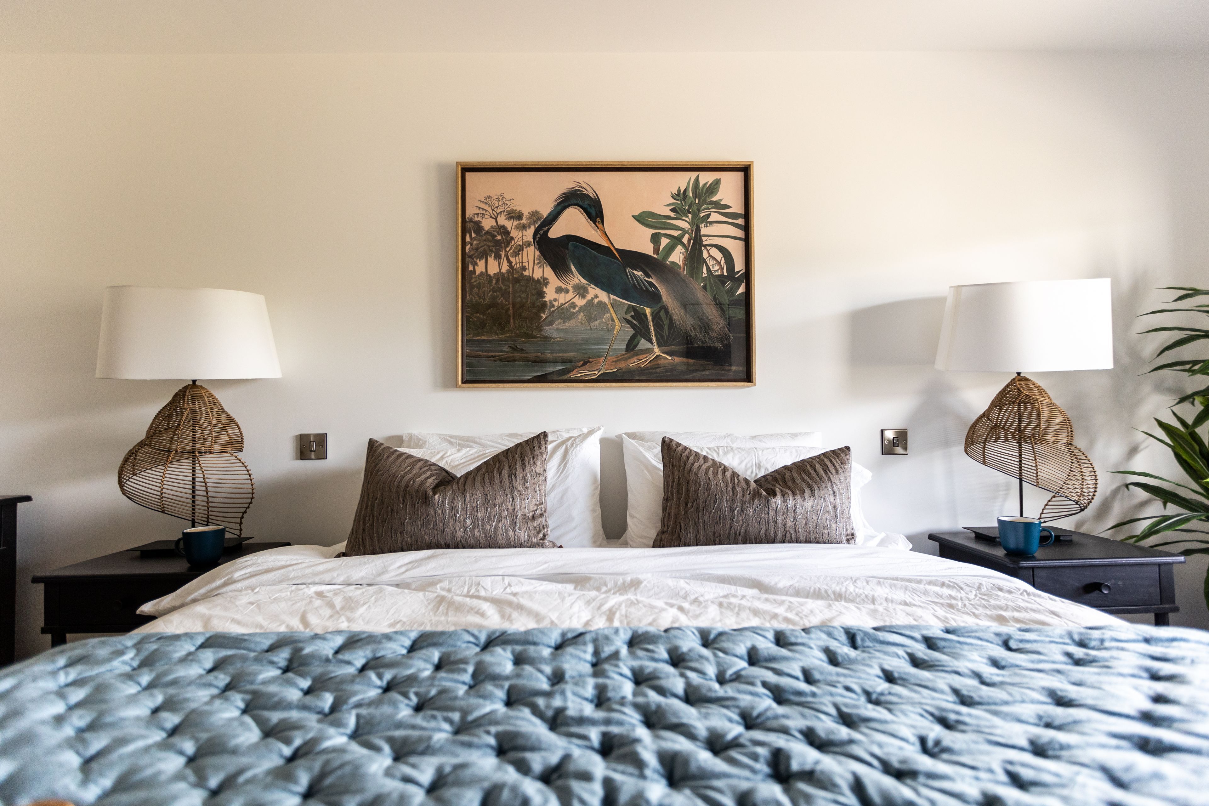 Habitación de hotel con cama, dos mesitas de noche, lámpara de pared, cuadro enmarcado y un ventanal grande.