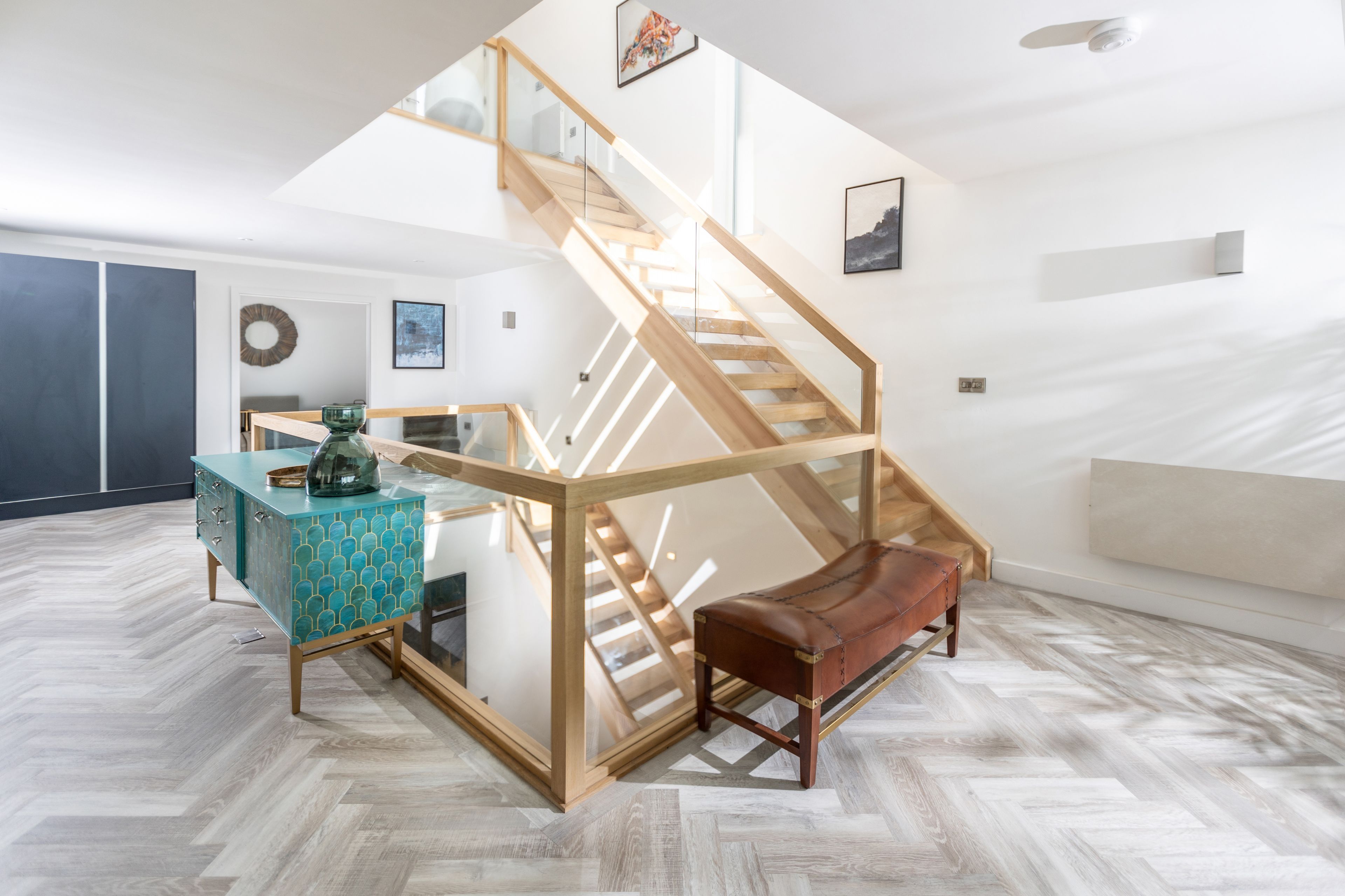 A modern interior with a wooden staircase, a glass railing, and a herringbone floor pattern.
