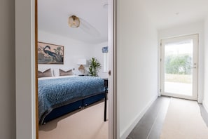 A bedroom with a bed, a painting, a lamp, and a door leading to a balcony. - Stunning Family Home Overlooking St Michaels Mount with hot tub (Marazion)