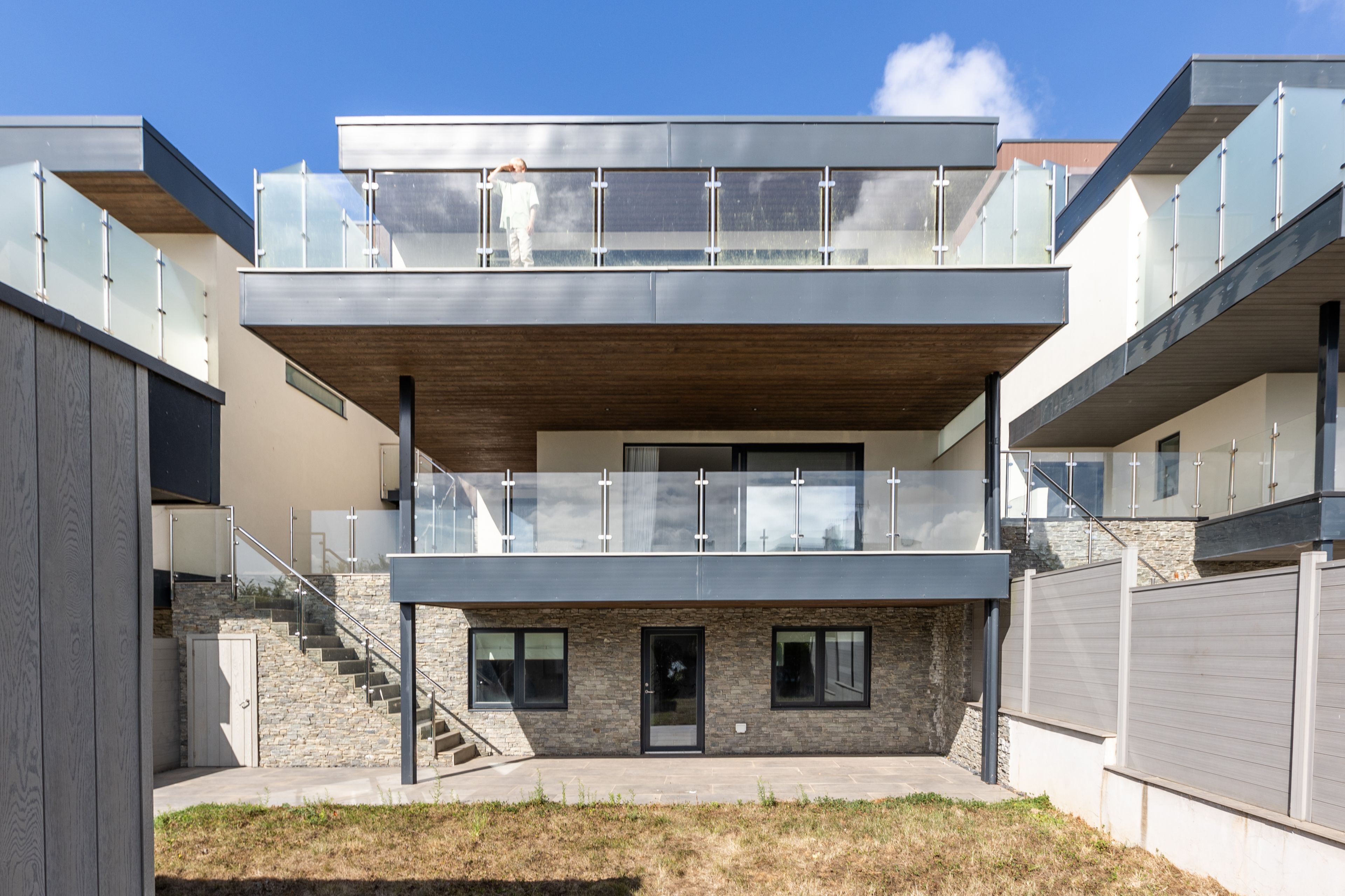 A modern multi-story residential building with a flat roof, large windows, and a balcony.