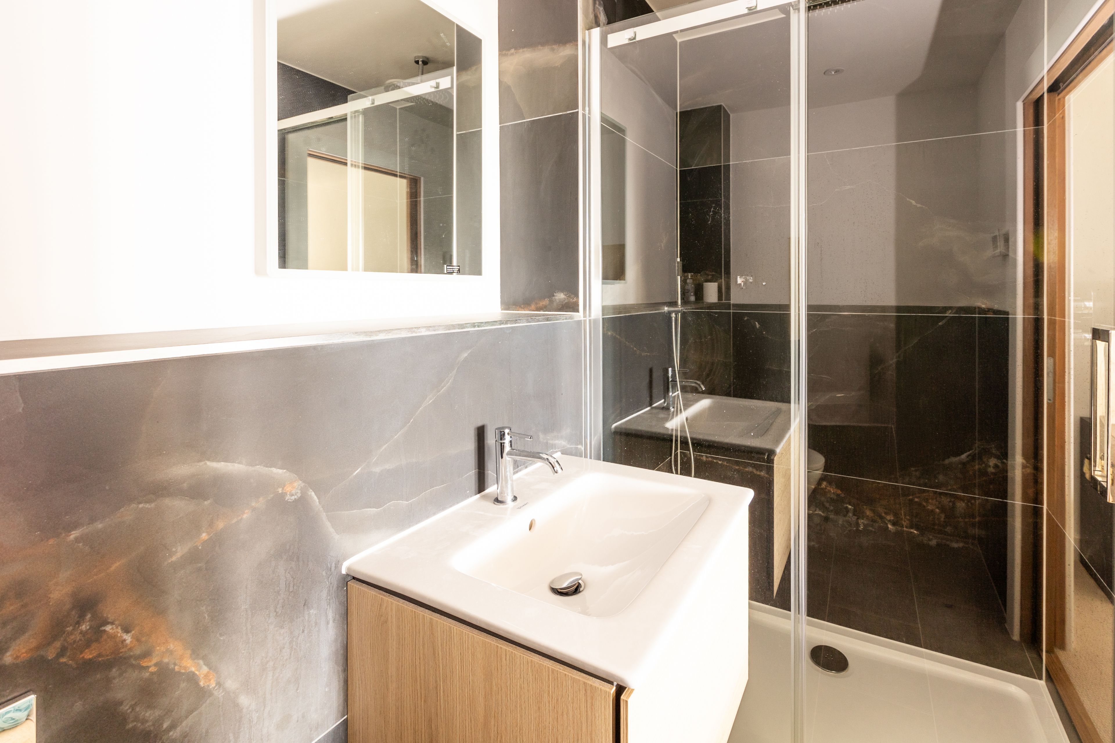 Une salle de bain moderne avec une douche à parois de verre, un lavabo blanc et un meuble en bois.
