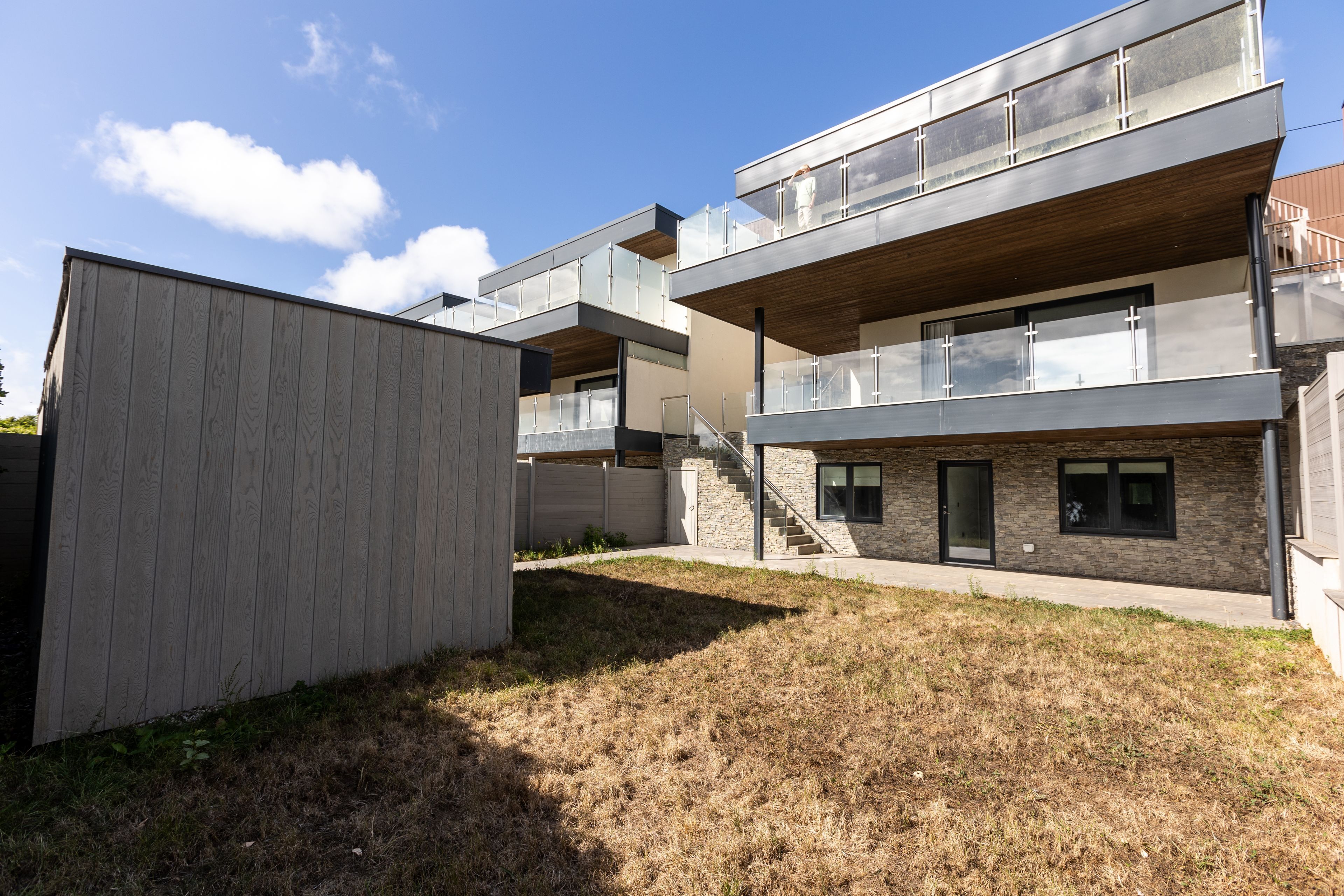 Een modern meerlaags gebouw met een plat dak, grote ramen en een houten terras.