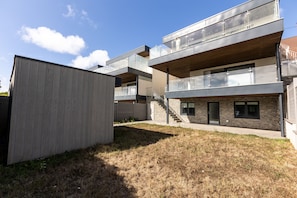 A modern multi-story building with a flat roof, large windows, and a wooden deck area.