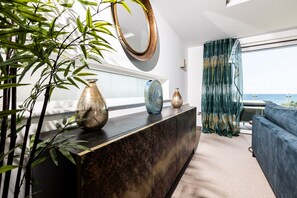 A modern living room with a dark marble console, decorative vases, a large mirror, and a view of the sea through sheer curtains.