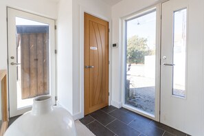 A hallway with a wooden door, a white door with a window, and a large white vase on the floor. - Stunning Family Home Overlooking St Michaels Mount with hot tub (Marazion)