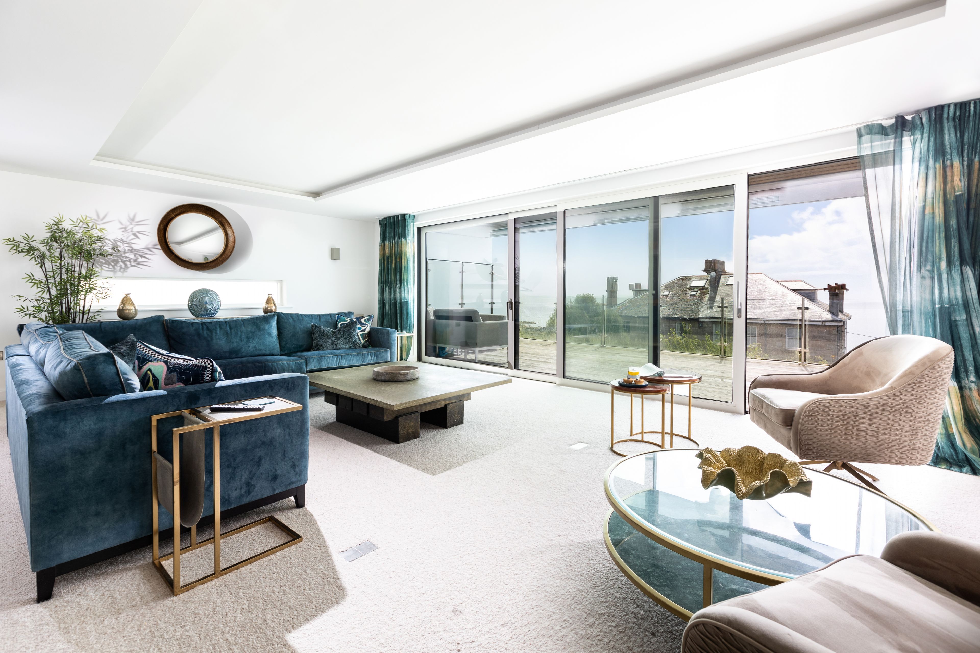A modern living room with a blue sofa, a glass coffee table, and a view of a cityscape through large windows.