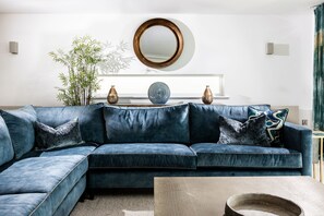 A modern living room with a sectional sofa, decorative vases, a mirror, and a potted plant. - Stunning Family Home Overlooking St Michaels Mount with hot tub (Marazion)