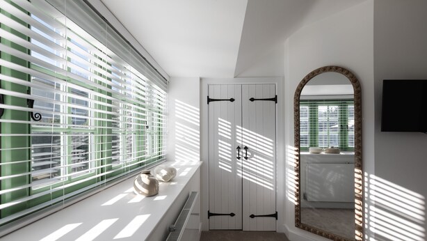Una habitación con radiador, ventana con persianas, armario y espejo.