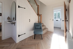 Ein modernes Interieur mit Fischgrätparkett, einem blauen Polsterstuhl, einer weißen Tür und einer Treppe mit Holzwertungen.