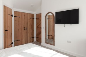 Ein Schlafzimmer mit einem Bett, einem Holzschrank, einem Spiegel und einem an der Wand befestigten Fernseher.