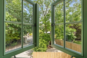 Blick durch ein grün gerahmtes Fenster auf ein Holzdeck und einen Garten.
