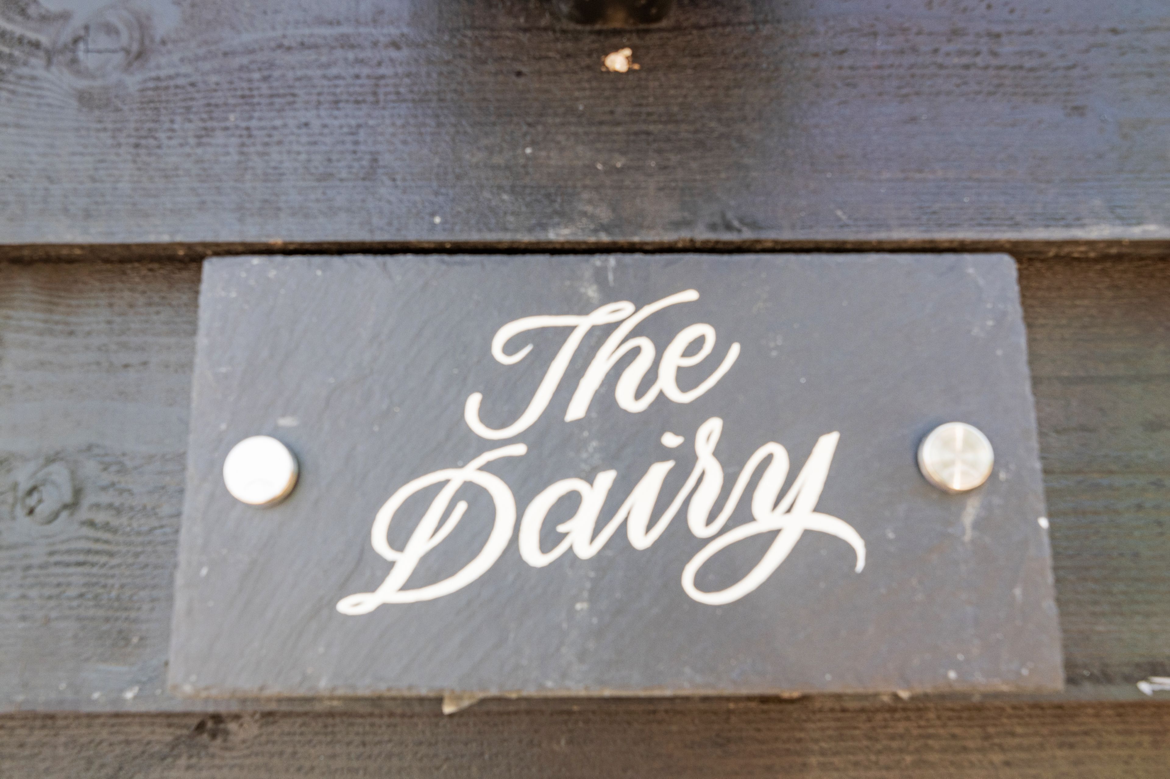 Een bord van leisteen met de tekst 'The Dairy' bevestigd op een houten ondergrond.