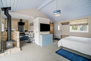 Une chambre avec un lit, une télévision, une cheminée et un coin cuisine doté de meubles en bois et d’une cuisinière.