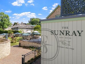 A sign for 'The Sunray Free House' with a logo, an entrance direction, and outdoor seating with umbrellas. - Wood-Fired Hot Tub & Pub Couples Retreat (Osmington, Weymouth)
