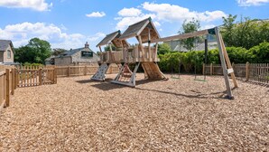 Une aire de jeux avec des structures en bois, une balançoire et une clôture en bois.