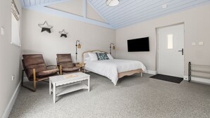 Une chambre à coucher avec un lit, deux chaises, une table blanche, un téléviseur et une porte.
