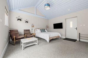 A bedroom with a bed, two chairs, a white table, a TV, and a door. - Wood-Fired Hot Tub & Pub Couples Retreat (Osmington, Weymouth)