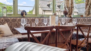 Un coin repas avec une table dressée pour six personnes, un canapé et une vue sur les maisons à travers de grandes fenêtres.