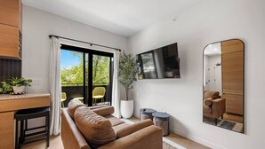 Una sala de estar moderna con un sofá, un televisor de pantalla plana, un espejo grande y un balcón con sillas amarillas.