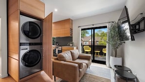 Un apartamento moderno con lavadora y secadora integradas, un sofá, zona de comedor con sillas amarillas y balcón con vistas.