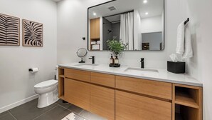 Un baño moderno con inodoro blanco, tocador de madera con espejo y lavabo.
