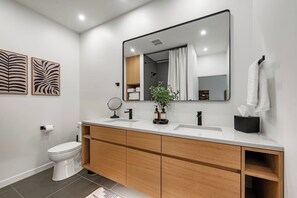 A modern bathroom with a white toilet, a wooden vanity with a mirror, and a sink.