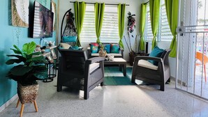 Una habitación con sofá, sillas, una mecedora, televisor y ventana con cortinas.