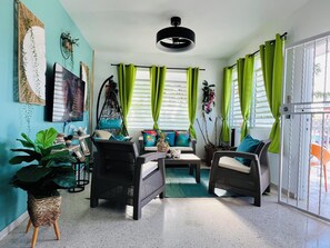 A room with a sofa, chairs, a hanging chair, a TV, and a window with curtains.