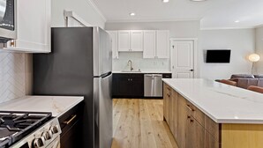 Et moderne køkken med en central ø, rustfrie hvidevarer og et backsplash med et fiskebensmønster.