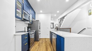 Een moderne keuken met blauwe kastjes, roestvrijstalen apparatuur en een wit aanrecht.