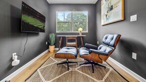 Een moderne kamer met een grote televisie, een comfortabele fauteuil, een bureau en een raam met uitzicht op bomen.