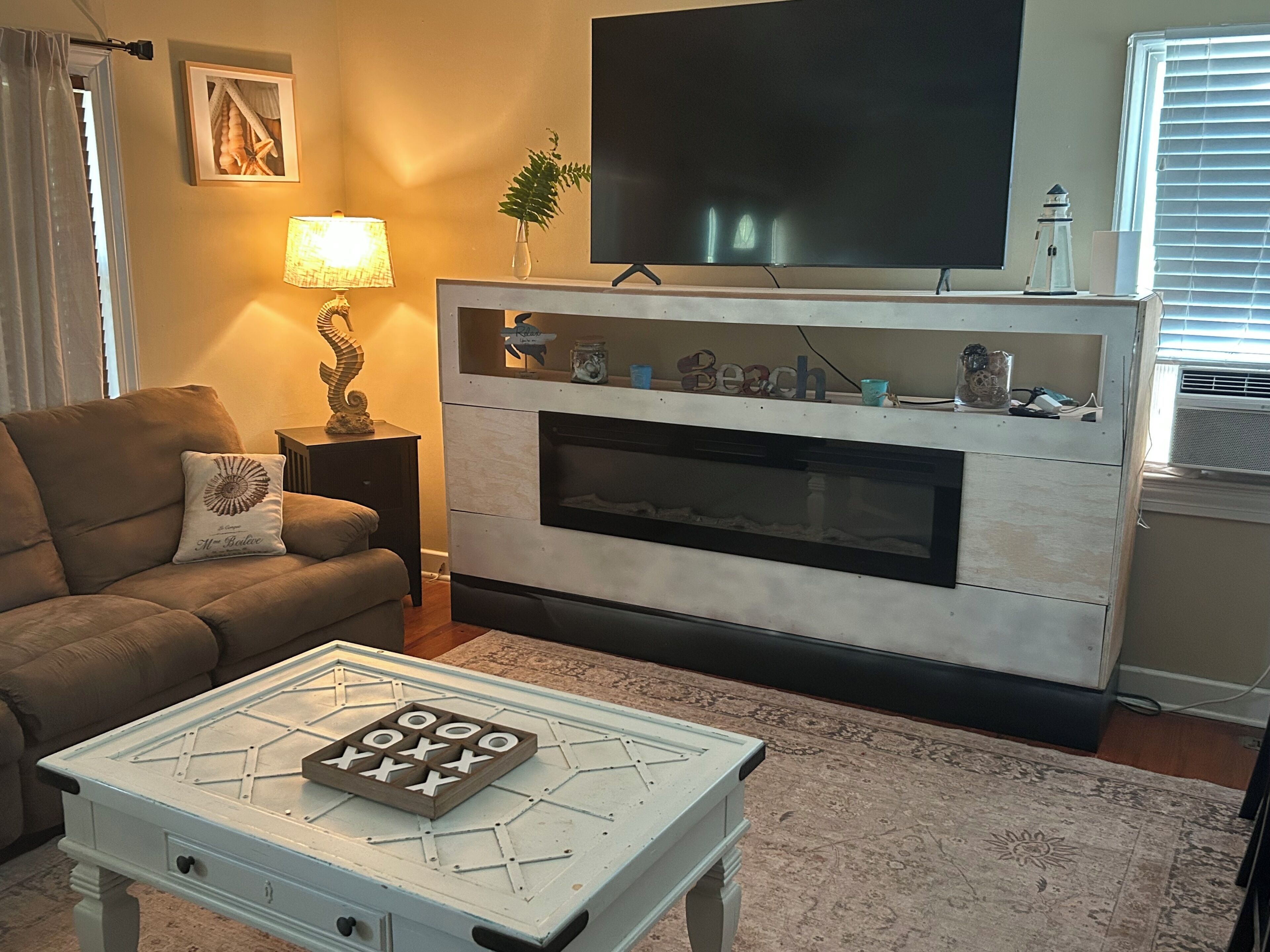 A living room with a sofa, a coffee table with a board game, a fireplace, a television, and a lamp.