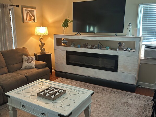 A living room with a sofa, a coffee table with a board game, a fireplace, a television, and a lamp.
