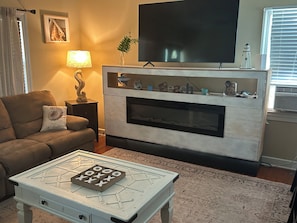 A living room with a sofa, a coffee table with a board game, a fireplace, a television, and a lamp.