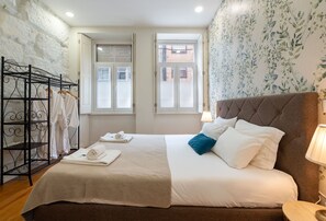 Ein Hotelzimmer mit einem Bett, einem Metallregal mit Handtüchern und zwei Fenstern.