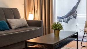 A modern living room with a sofa, a coffee table, a lamp, and a view of a hammock outside. - Patio de Santa Catarina (N77) (Porto)
