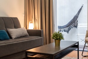 Ein modernes Wohnzimmer mit einer Couch, einem Couchtisch, einer Lampe und Blick auf eine Hängematte draußen.