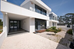 Un bâtiment moderne à deux étages, doté d’un patio couvert, de grandes fenêtres et d’un jardin agrémenté de petits arbres et d’arbustes.