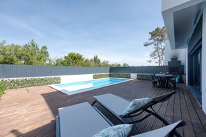 Une terrasse en bois avec une piscine, des chaises longues et un coin repas.