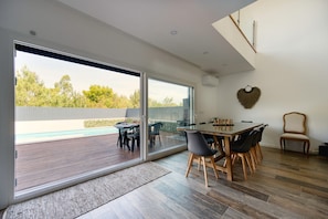 Een moderne eetruimte met een glazen schuindeur naar een terras, een houten tafel en stoelen.