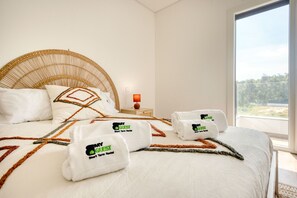 Une chambre d’hôtel avec un grand lit, une tête de lit en osier, une table de chevet avec une lampe et une vue sur l’extérieur.