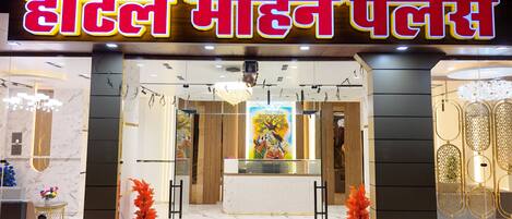 A hotel entrance with a prominent sign, a central chandelier, and a decorative wall painting.