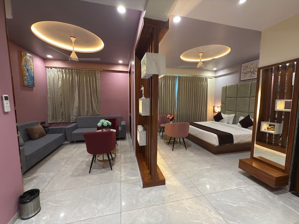 A modern hotel room with a sofa, a dining table, a chair, a bed, and a mirror. - HOTEL MOHAN PALACE (Khatoo)