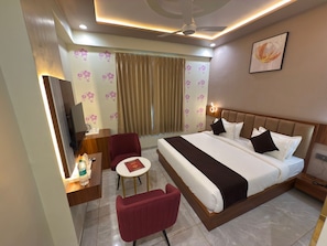 A hotel room with a bed, a desk with a chair, a TV, and a small table with a chair. - HOTEL MOHAN PALACE (Khatoo)