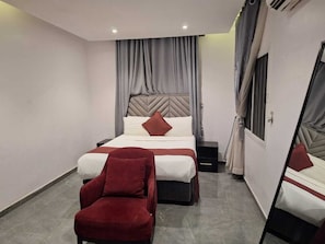 Habitació d'hotel amb un llit, una cadira, una taula de nit i un mirall.