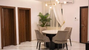 Un comedor con una mesa redonda, cuatro sillas, una araña y una planta en maceta.