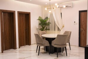 A dining area with a round table, four chairs, a chandelier, and a potted plant. - Sun Heaven Residence Lekki (Lekki)